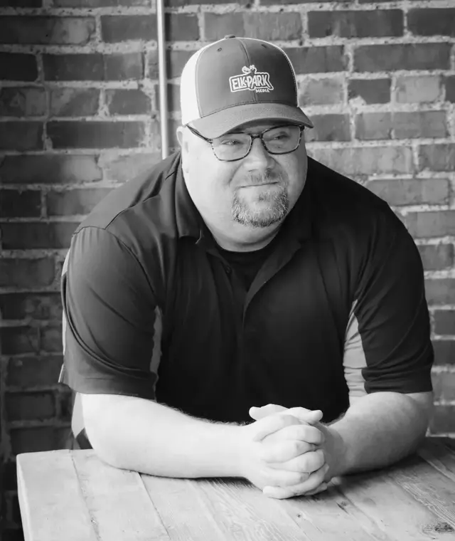 Jason Elkins of 100 Cups Consulting, leaning on a table in front of a brick wall